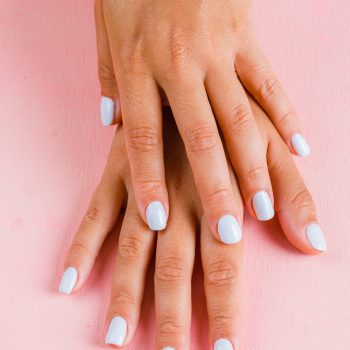 Self care concept with female white manicure on pink background flat lay.