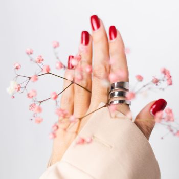 Soft gentle photo of woman hand with big ring red manicure hold cute little pink dried flowers isolated on white background, spring mood.